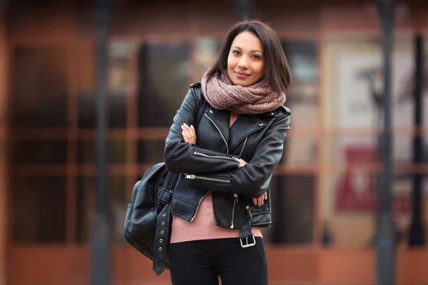 Stylish woman wearing a black leather jacket accessorized with a silk scarf, layered necklaces, and a crossbody bag.
